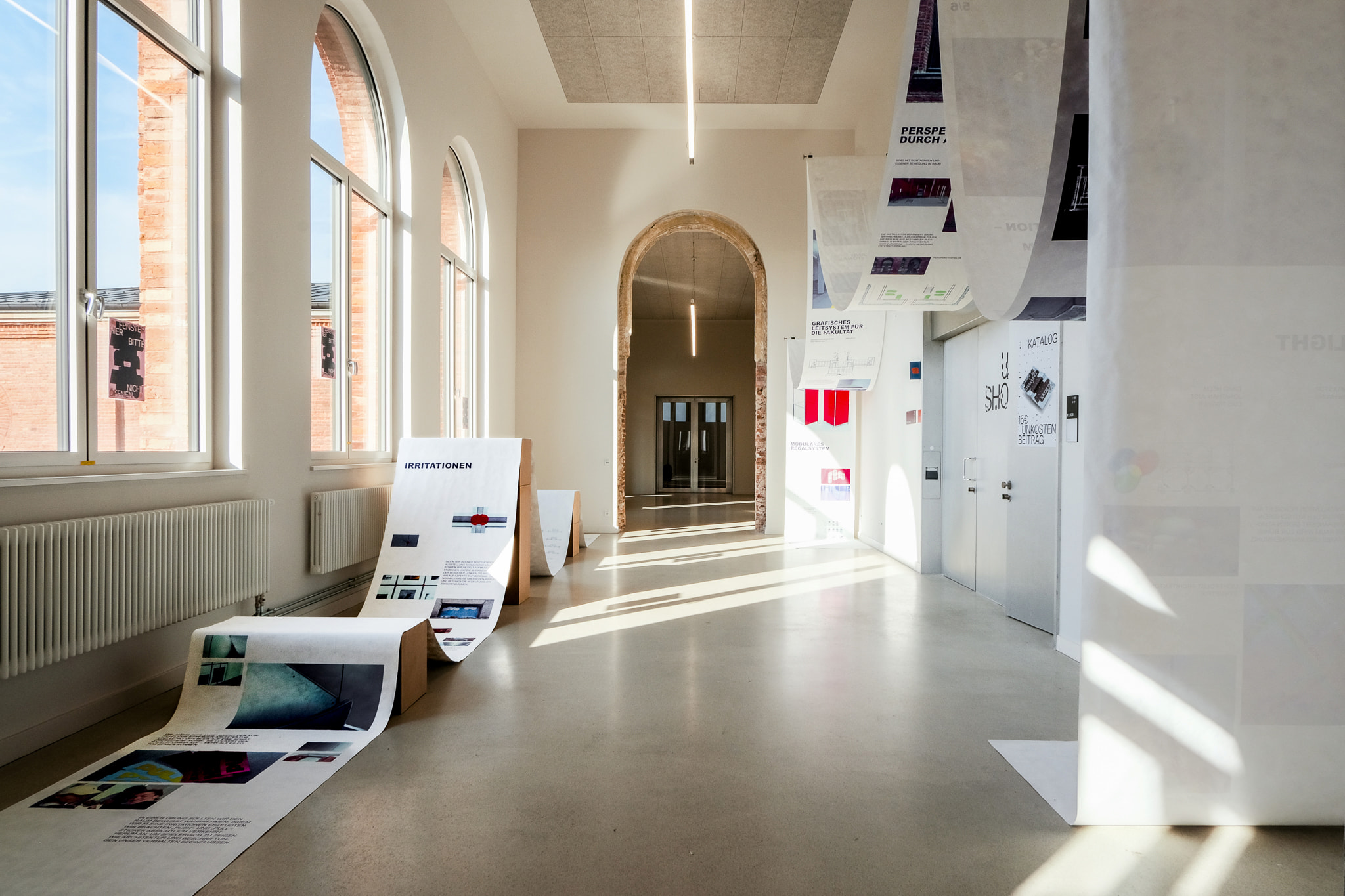 A high room with a 30m banner hung up in waves, on the left side and another banner on the right side, also draped in waves. The left banner has images on it, the right banner text, documenting a course called temporary room installation